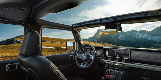 Display The front row in the 2025 Jeep Wrangler focusing on the open sunroof, steering wheel, Uconnect touchscreen and dash