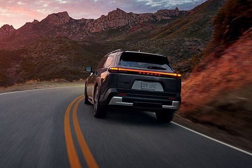 A 2026 Subaru Trailseeker EV SUV drives on a winding desert road at sunset, mountains in the background